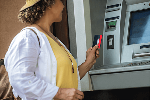 Woman in sunhat standing next to ATM holding credit card in hand.