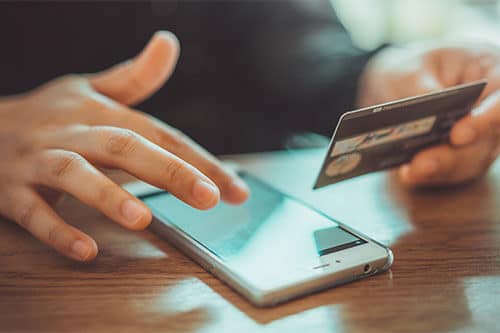 Person sitting at table with phone screen in front of them and holding credit card in hand.