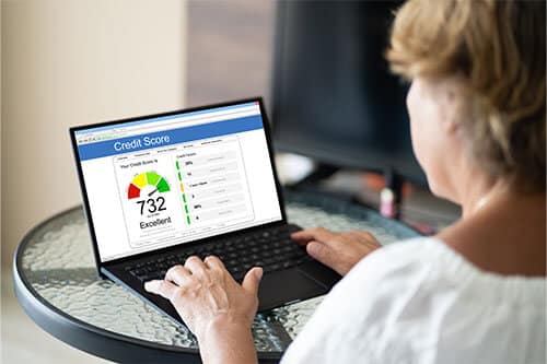 Woman sitting at small round table with laptop open to credit score monitoring screen.
