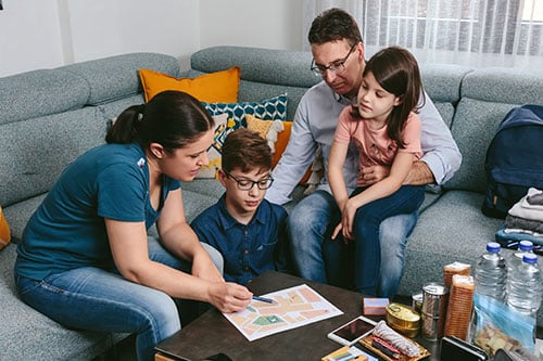 Family of four sitting around coffee table in living room with emergency supplies discussing exit plan.