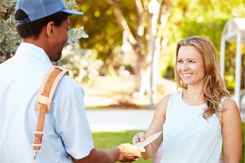 Postman handing woman envelope outside on sunny day.