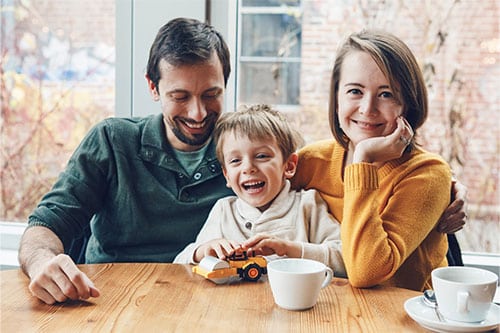 Family of three smiling and happy sitting at kitchen table.