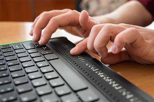 Disabled person using braille on computer keyboard.