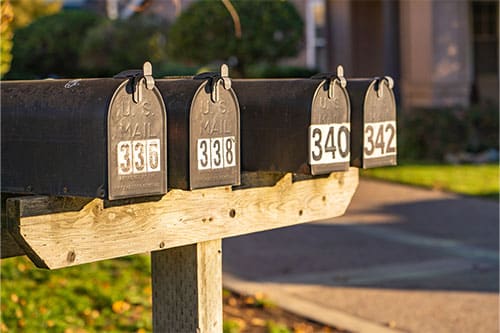 Row of of mailboxes with large numbers on the front at the end of driveway.