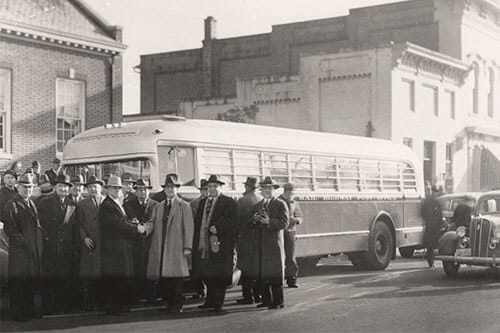 Old photograph of mailworkers in long trenchboats and hats standing next to mail bus.