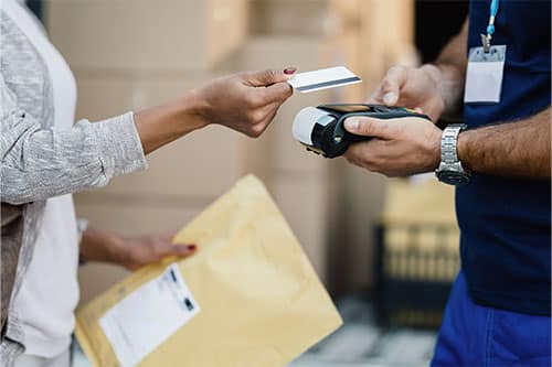 Woman standing holding credit card out to man in front of her holding payment reader.