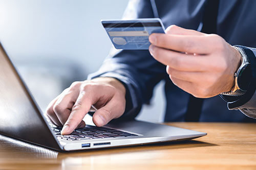 Man working on laptop keyboard and holding credit card in hand.
