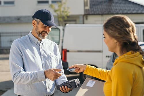 Woman holding out credit card to delivery man to pay on hand held device.