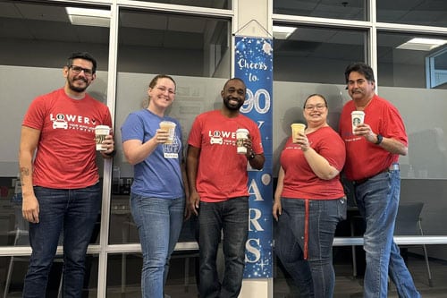 Five coworkers standing together for photo with coffee cups in hands.