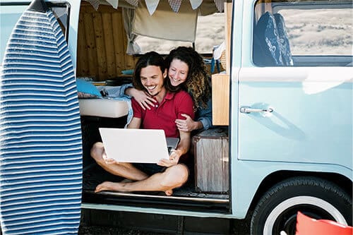 Couple sitting in back door entry of van looking at laptop.