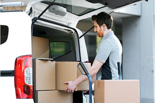 Delivery man unloading boxes from back of van onto forklift.