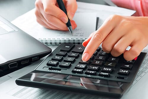 Person typing on calculator and writing in notebook at desk.
