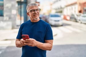 Man in glasses and blue shirt smiles while holding a red smartphone on a city street